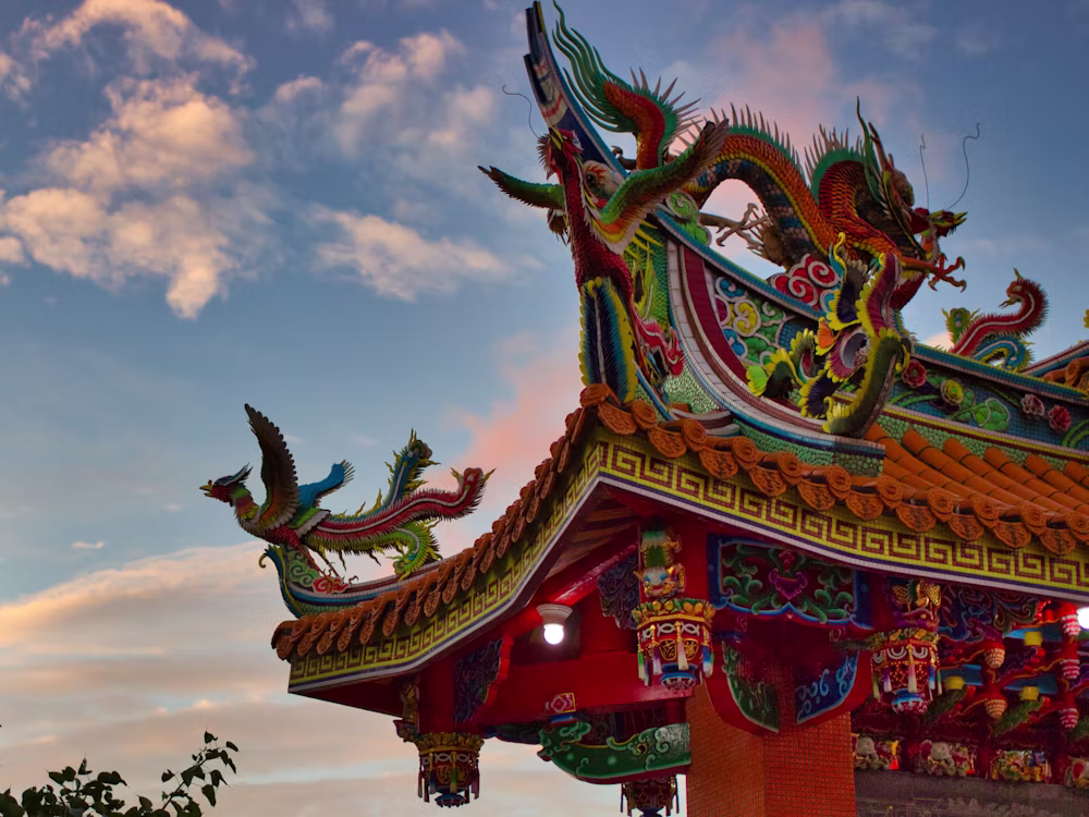 Ornate dragon and phoenix figures on a colourful Taiwanese temple roof against a sunset sky